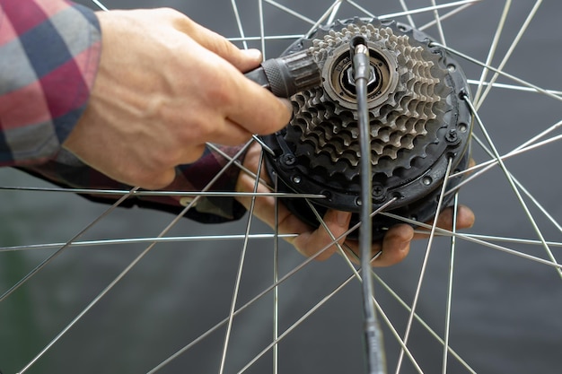 The bike mechanic installs a new cassette on the motor wheel Repair of electric bicycles Mechanic's hand and wrench closeup Replacement of wornout equipment on a mountain bike