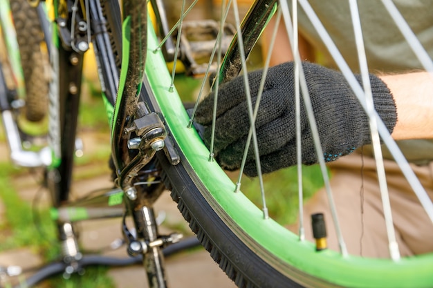 Bike mechanic man repairs bicycle in bicycle repair shop, outdoor. Hand of cyclist bicyclist examines, fixes modern cycle transmission system. Bike maintenance, sport shop concept.