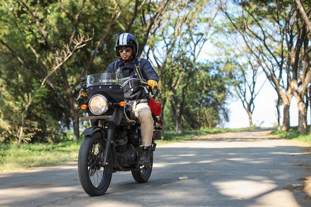 Biker in black leather outfit riding motorbike along countryside road on bright summer day