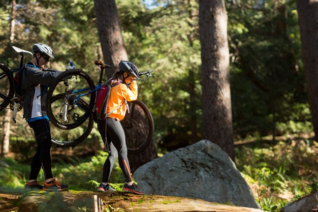 Coppie del motociclista che tengono il loro mountain bike e che camminano nella foresta