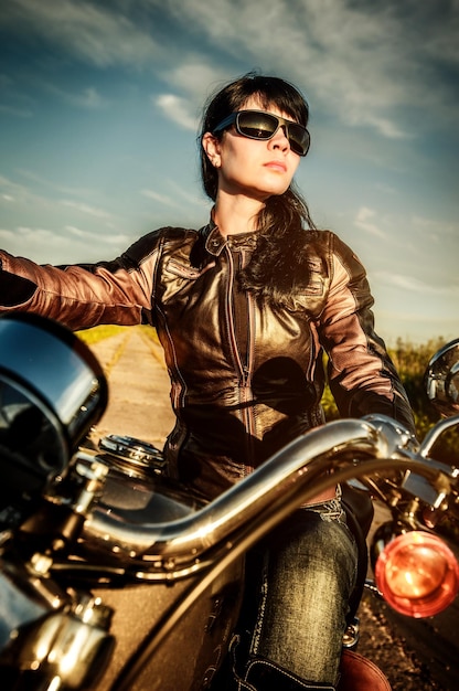 Biker girl in a leather jacket on a motorcycle looking at the sunset.