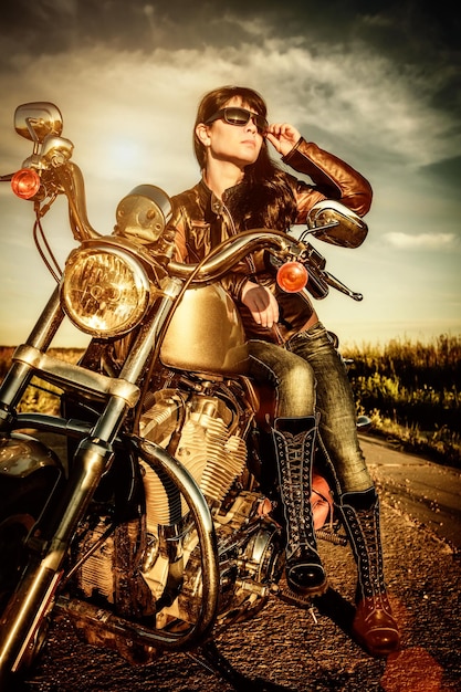 Biker girl in a leather jacket on a motorcycle looking at the sunset.