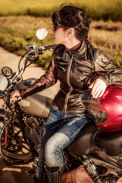 Biker girl in a leather jacket on a motorcycle looking at the sunset.