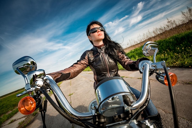 夕日を見ているオートバイの革のジャケットのバイカーの女の子。