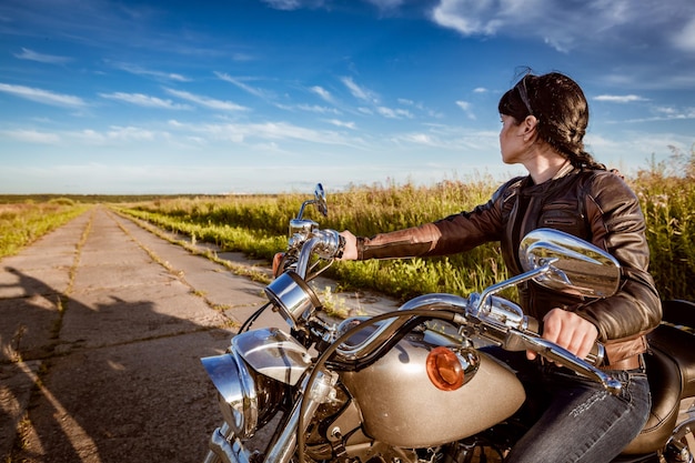 Foto ragazza del motociclista in una giacca di pelle e occhiali da sole che si siede sulla motocicletta