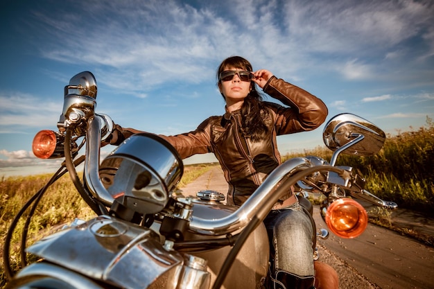 Biker girl in a leather jacket and sunglasses sitting on motorcycle