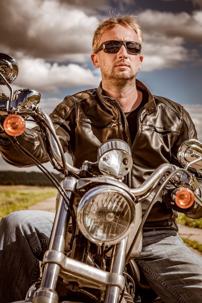 Biker man met een leren jas en zonnebril zittend op zijn motorfiets