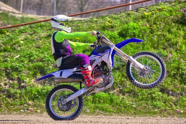 Biker on motorcycle stunts while driving on the rear wheel side view