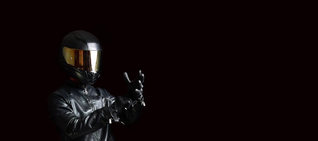 Biker motorcyclist in a protective motorcycle jacket with gloves and a helmet on a dark background.