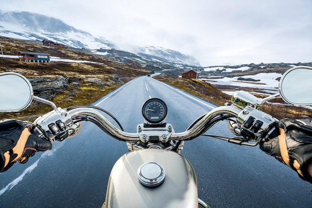 Biker rides a motorcycle on a slippery road through a mountain pass in Norway. Around the fog and snow. First-person view.