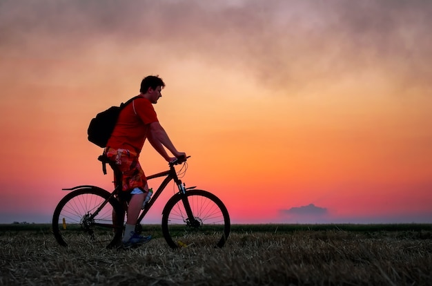 Biker with bicycle on the field during sunrise