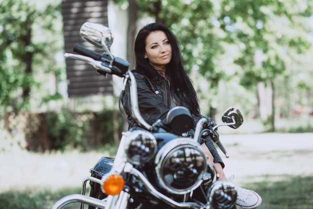 biker woman in a leather jacket on a motorcycle looks into the distance on a summer sunny day
