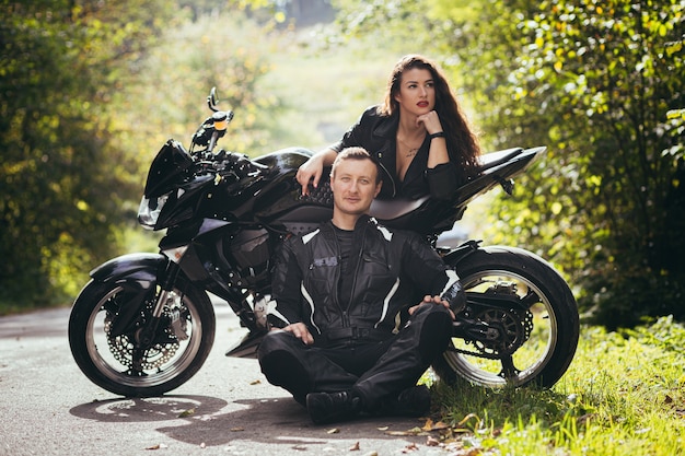 Байкеры в кожаной одежде, мужчина и женщина, сидящие на черном спортивном мотоцикле в лесу