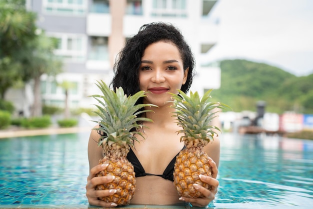Bikini young woman showing pineapple pineapple fruit woman\
smiling healthy and joyful mixedrace asian caucasian model with\
pineapple