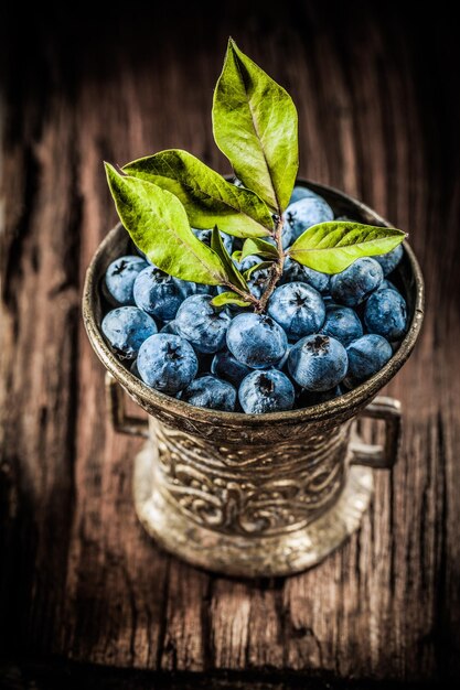 Bilberries in metal bowl on vintage wooden board vertical view