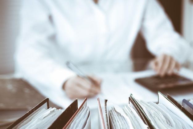 Binders of papers waiting to process by bookkeeper woman or financial inspector, close-up. Business portrait. Audit or tax concepts.