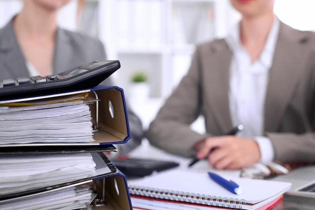 Binders with papers are waiting to be processed with businessman and secretary back in blur Internal Revenue Service inspector checking financial document