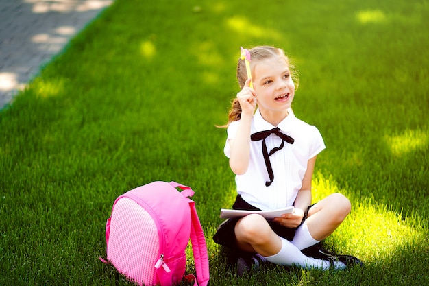 Bingo. la piccola ragazza della scuola con lo zaino rosa che si siede sull'erba dopo le lezioni e le idee di pensiero, ha letto il libro e studia le lezioni, scrivendo le note, l'istruzione e l'apprendimento del concetto