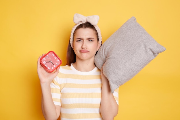 Binnen schot van trieste vrouw met wekker ontwaken hard vroeg dragen casual gestreepte tshirt poseren geïsoleerd op gele achtergrond Blanke vrouw heeft niet genoeg slaap wil meer rust in het weekend