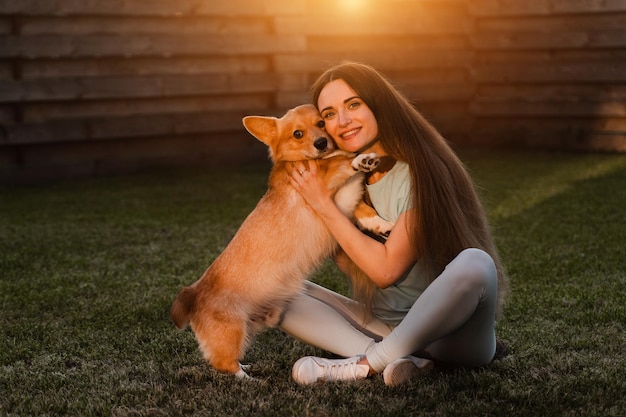 Binnenlandse corgi-hond met meisjeseigenaar jonge vrouw zittend op het gras en knuffel welsh corgi pembroke lifestyle met binnenlandse speelse hond