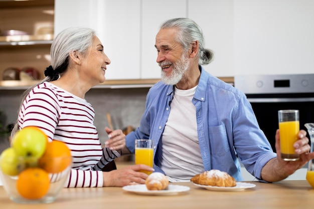 Binnenlandse ochtend gelukkige senior echtgenoten chatten en lachen tijdens het ontbijt in de keuken