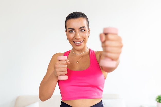 Binnenlandse training met gewichten Positieve zwarte dame die oefeningen doet met halters die haar lichaam thuis versterken Glimlachende jonge vrouw die aan haar biceps-spieren werkt en gezond blijft