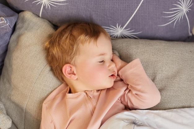 Binnenopname van een babymeisje liggend op een bed slapend op roze lakens liggend met gesloten ogen rustend na een zeer actieve dag