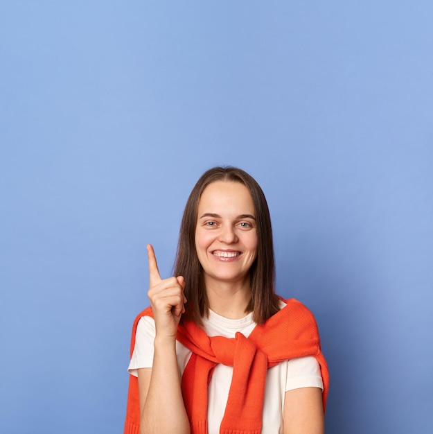 Binnenopname van glimlachende slimme slimme vrouw die casual kleding draagt, opgestoken vinger omhoog met een idee kijkend naar de camera met brede glimlach staande geïsoleerd over blauwe achtergrond