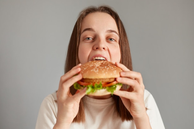 Binnenopname van hongerige vrouw met bruin haar die cheeseburger bijt met plezier hamburger bestellen hamburger bestellen voor afhaalmaaltijden in fastfoodrestaurant genieten van heerlijke smaak