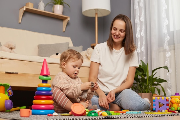 Binnenopname van moeder en kind spelen op de vloer in de kinderkamer moeder en klein meisje brengen samen tijd door kind doet haar sokken uit vrouwtje glimlacht gelukkig