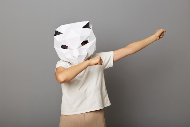 Binnenopname van vrouw met kattenpapieren masker en wit T-shirt poseren geïsoleerd over grijze achtergrond opgeheven handen in dab dans pose internet meme succes vieren