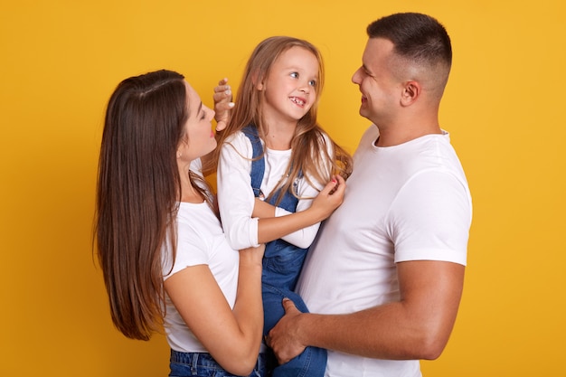 Binnenschot van gelukkige jonge familie met één kind dat en bij camera bekijkt glimlacht