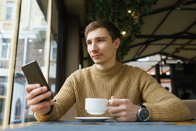 Binnenschot van jonge mensenzitting in de tekstbericht van de koffiewinkellezing op mobiele telefoon.