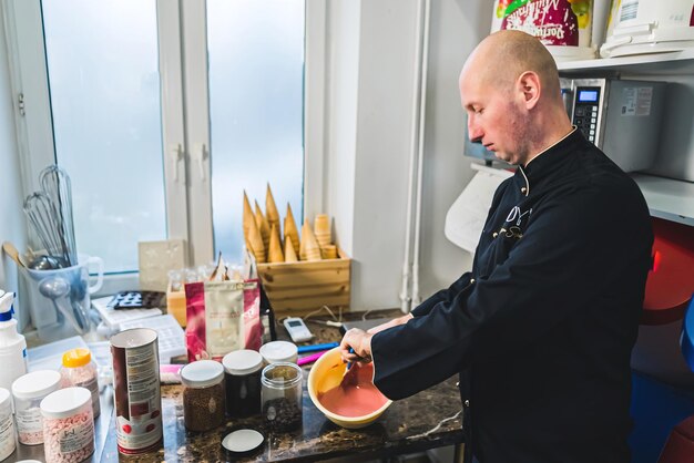 Binnenshuis shot van professionele chef-kok die snoep voorbereidt kale blanke man die robijnrode beslag in een kom mengt