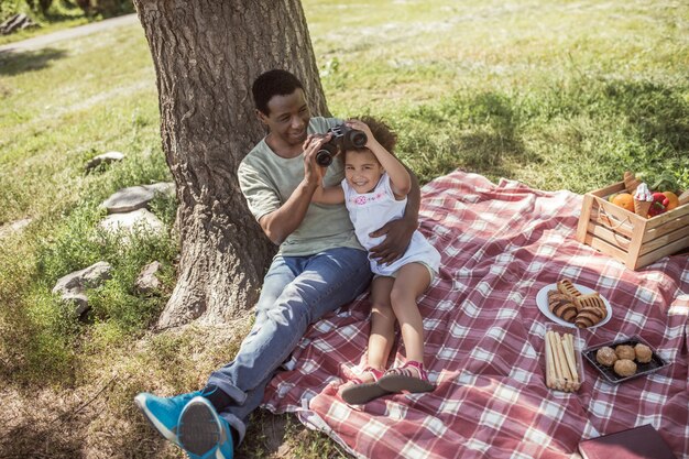 Binocular. Dark-skinned man showing a binocular to his daughter