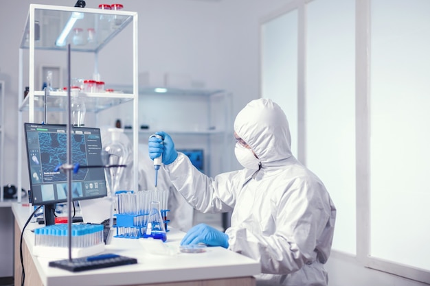 Scienziato biochimico che preleva un campione di soluzione blu con una pipetta per sviluppare il vaccino. chimico in un moderno laboratorio che fa ricerca utilizzando l'erogatore durante l'epidemia globale con covid-19.