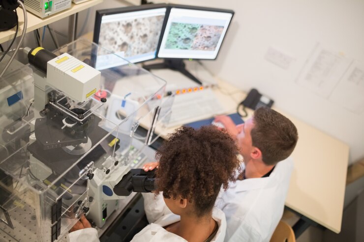 Photo biochemistry students using large microscope and computer