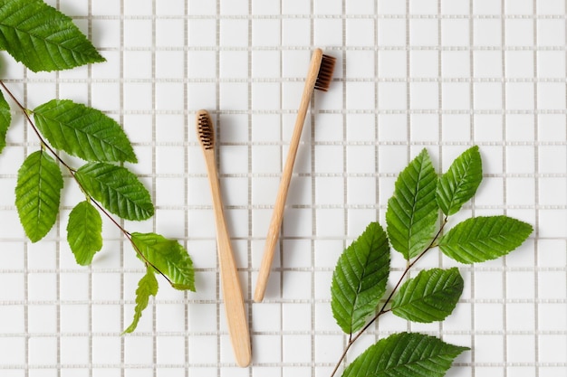 사진 녹색 식물 가지가 있는 흰색 모자이크 배경의 생분해성 대나무 칫솔 친환경 지속 가능한 생활 방식 치과 치료 개념