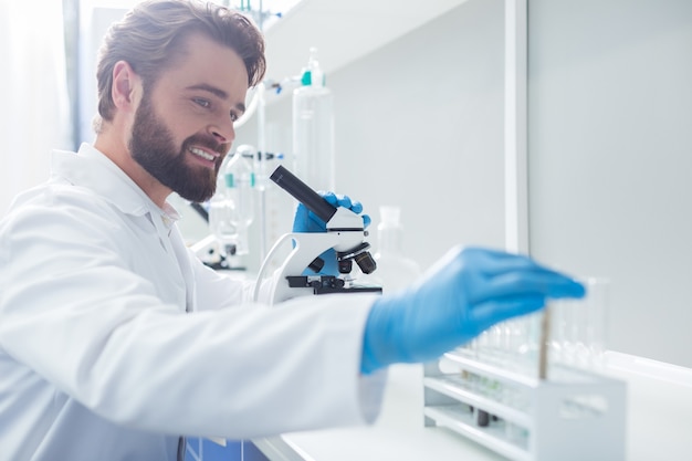 생물학적 연구. 생물학적 연구를 수행하는 동안 현미경을 들고 시험관을 복용하는 긍정적 인 똑똑한 남성 생물 학자