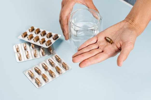 Biologisch actieve supplementen pil in de hand en glas water en blaren met andere tabletten op blauwe achtergrond Goed voedingsconcept Set van mulvitamine aminozuren mineralen