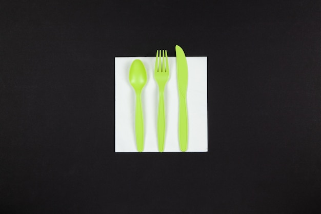Biologisch afbreekbare herbruikbare recyclebare groene vork, lepel, mes gemaakt van maïszetmeel gelegd op wit servet op zwarte achtergrond