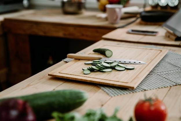 Foto biologisch groentenassortiment op houten keukentafel met snijplank en mes. vegetarisch recept gezonde maaltijd lifestyle concept. close-up op gehakte plakjes komkommer op houten kookplaats