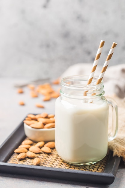 Biologische amandelmelk in een glas met amandelen op een grijze ondergrond