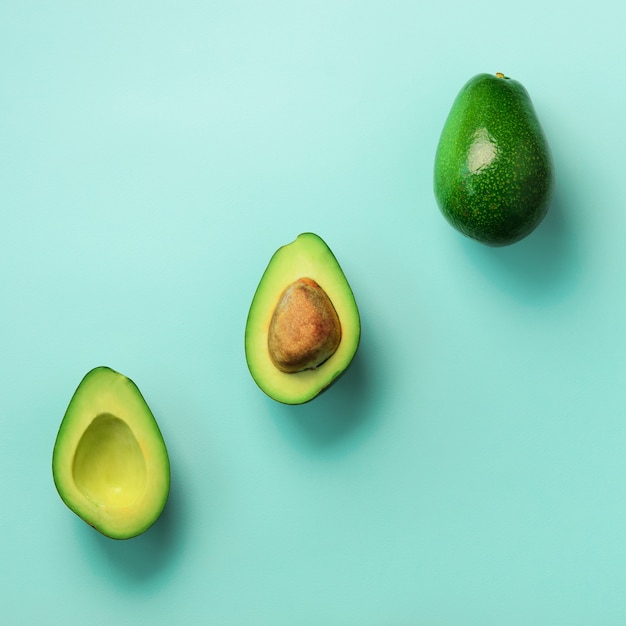 Biologische avocado met zaad, avocado helften en hele vruchten op blauwe achtergrond. Groen avocado patroon in minimale platte lay-stijl.