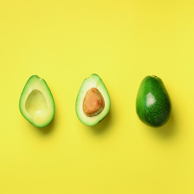 Biologische avocado met zaad, avocado helften en hele vruchten op gele achtergrond. Groen avocado patroon in minimale platte lay-stijl.