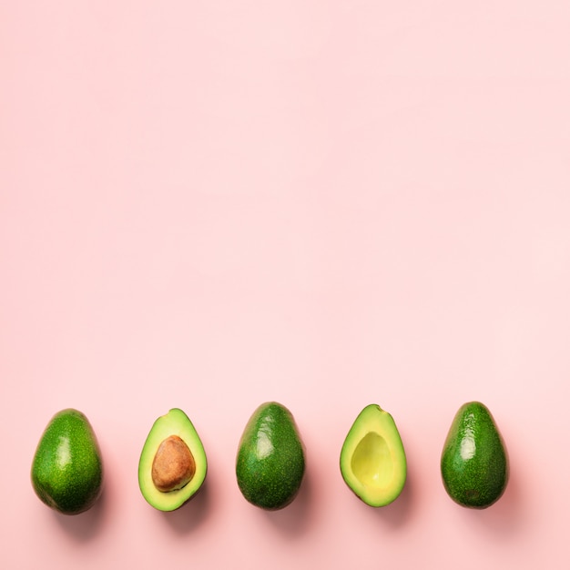 Biologische avocado met zaad, avocado helften en hele vruchten op roze achtergrond. Groen avocado patroon in minimale platte lay-stijl.