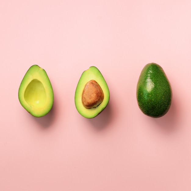 Biologische avocado met zaad, avocado helften en hele vruchten op roze achtergrond. Groen avocado patroon in minimale platte lay-stijl.