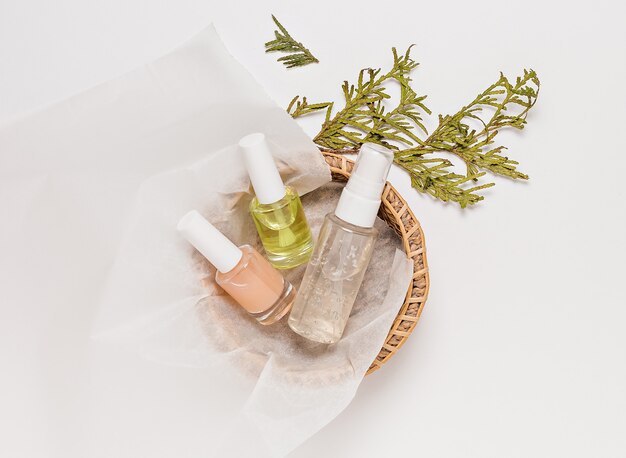 Foto biologische cosmetica met plant. platliggend, bovenaanzicht helder glazen pompflesje, penseelpotje, vochtinbrengende serumpotje in een papieren mandje op een witte achtergrond. natuurlijke cosmetica spa