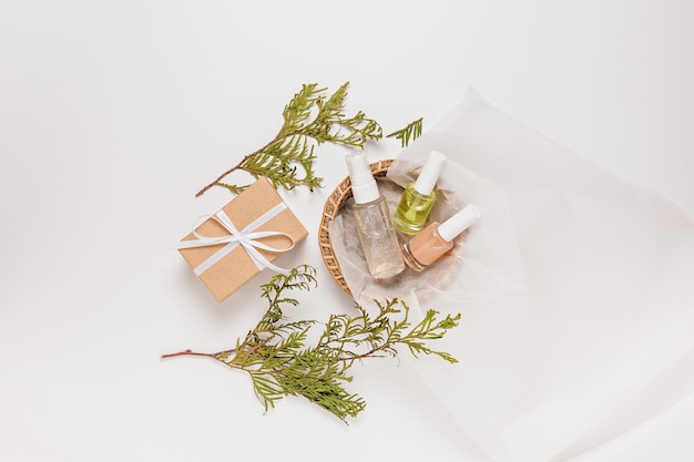 Biologische cosmetica met planten en geschenken voor de vakantie. Platliggend, bovenaanzicht helder glazen pompflesje, penseelpotje, vochtinbrengende serumpotje in een papieren mandje op een witte achtergrond. Natuurlijke cosmetica SPA