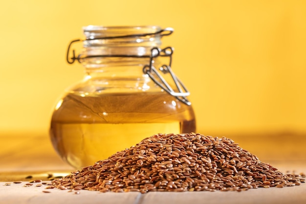 Biologische lijnzaadolie in een glazen pot met hele lijnzaad op een levendige oranje achtergrond